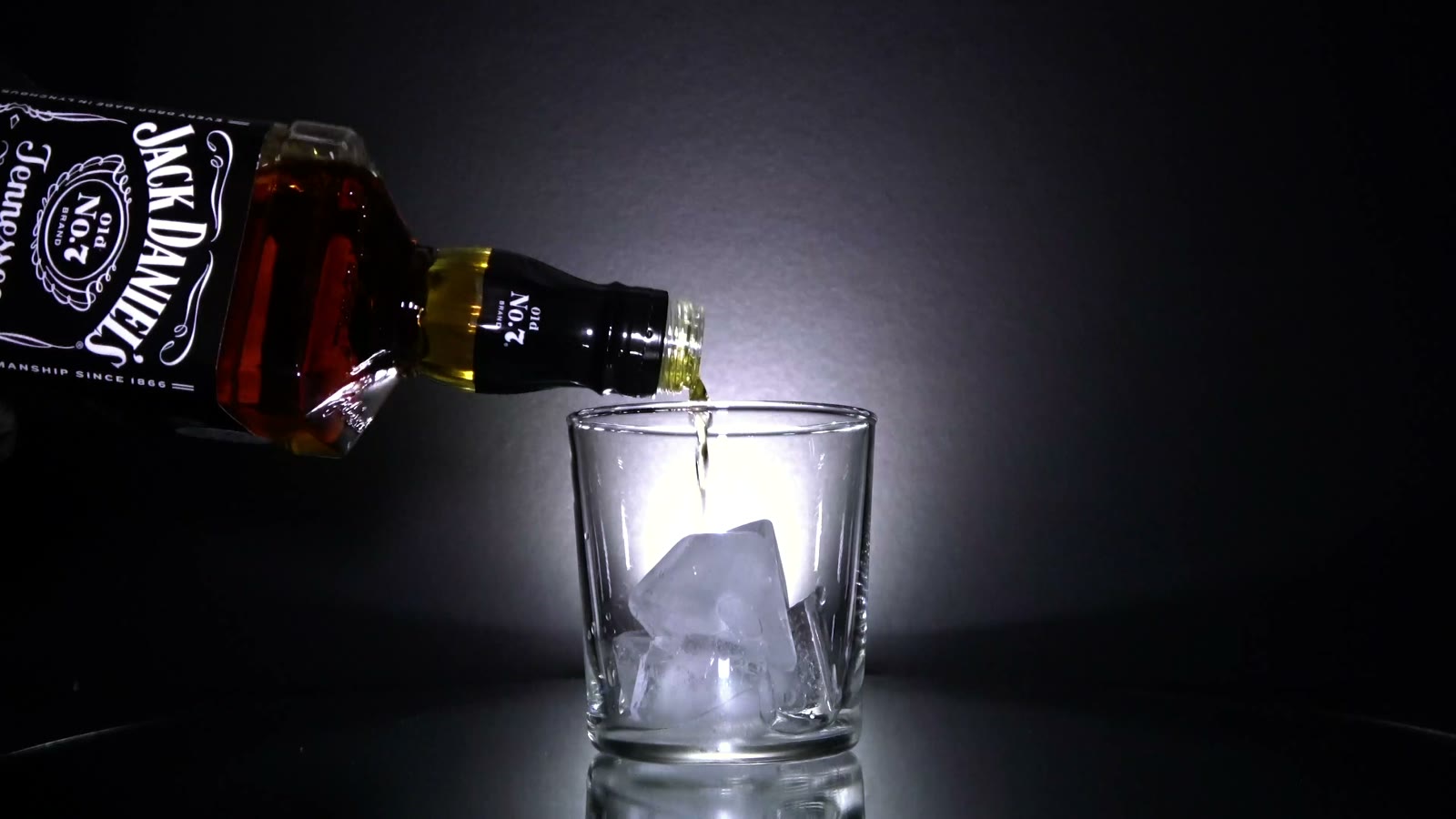 Jack Daniel’s whiskey pouring over ice in a glass, dramatic light